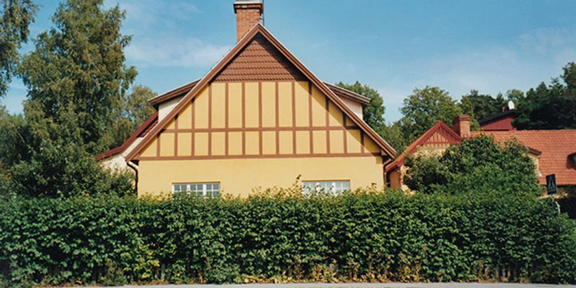 Husgaveln på ett gult hus med bruna detaljer, omgiven av grönska.