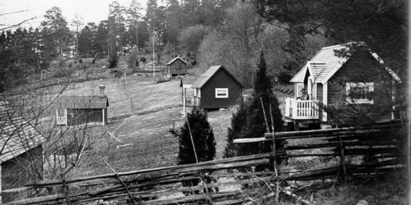 Ett svartvitt foto av en koloni med stugor.