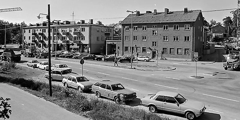 Ett svartvitt foto av en stadsgata omgiven av parkerade bilar.