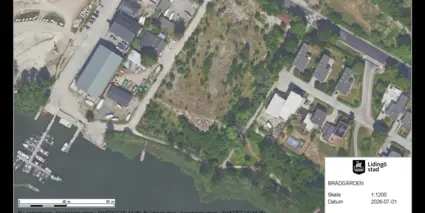 En flygbild över ett område med natur och byggnader intill ett vattenområde.