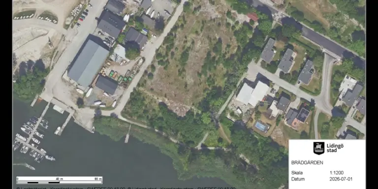 En flygbild över ett område med natur och byggnader intill ett vattenområde.