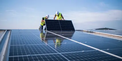 Två män i gula västar installerar solceller på ett tak.