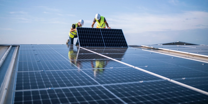 Två män i gula västar installerar solceller på ett tak.