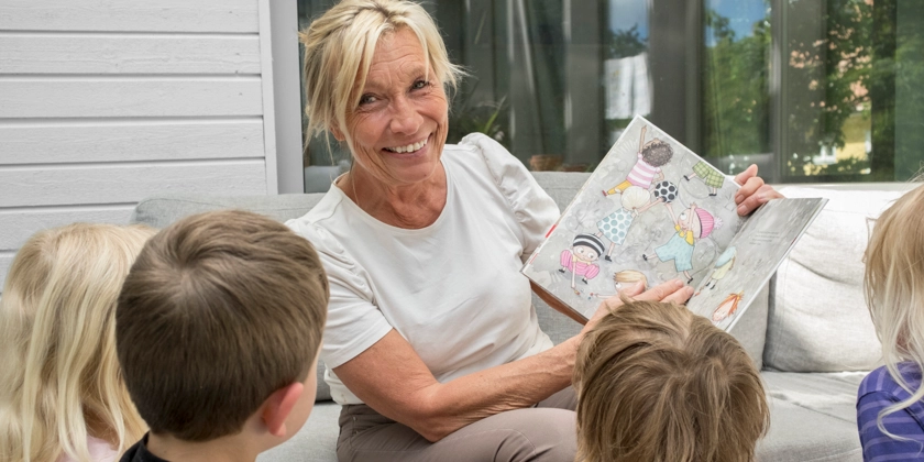 En kvinna som sitter i en soffa och läser en bok för barnen.