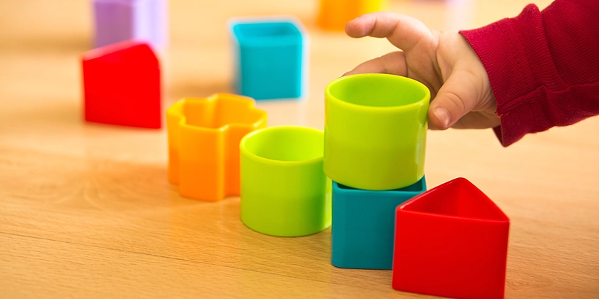 Ett barns hand som leker med färgglada plastklossar.