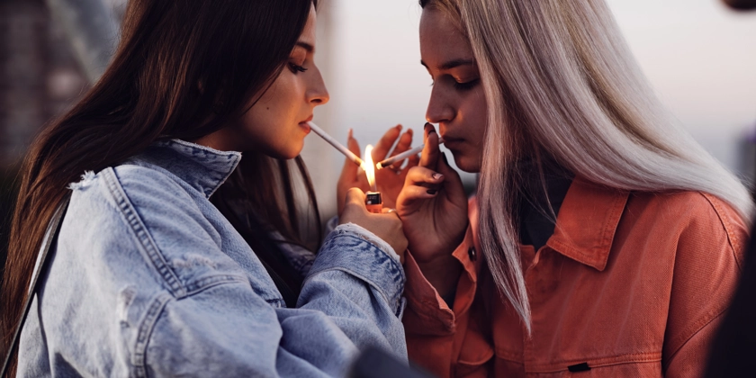 Två kvinnor som står bredvid varandra och röker cigarett.