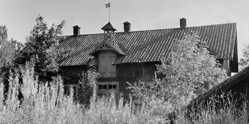 Ett svartvitt foto av en gammal ladugård med höloftsdörrar.