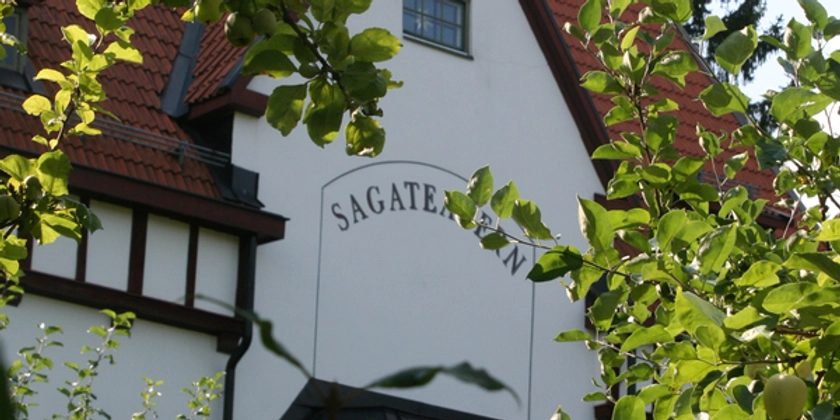 Fasaden på Sagateatern med grönskade äppelträd i förgrunden.