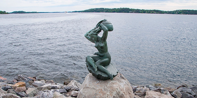 En skulptur som sitter på en sten vid vattnet.