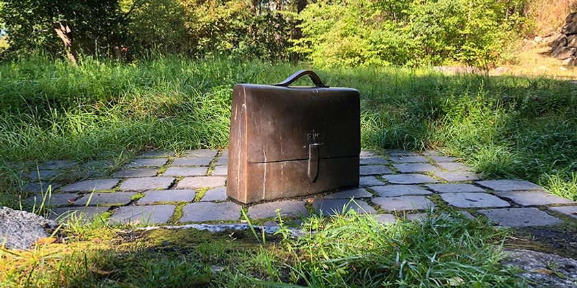 Skulptur av Raoul Wallenbergs attachéväska i bron står på en stenläggning med gräs runtom