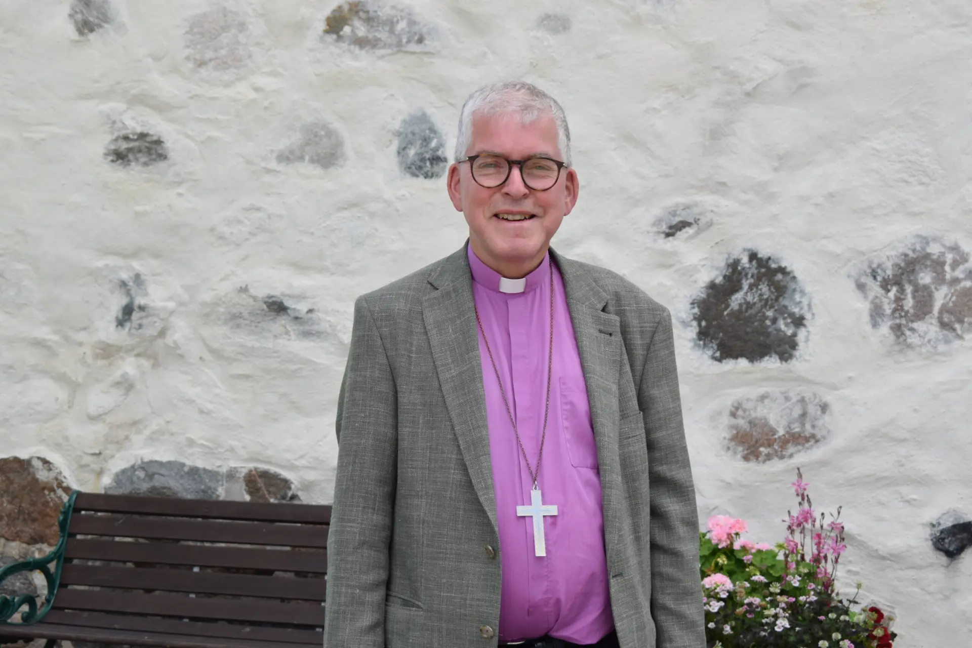 Biskop i grå kavaj framför kyrka