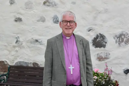 Biskop i grå kavaj framför kyrka