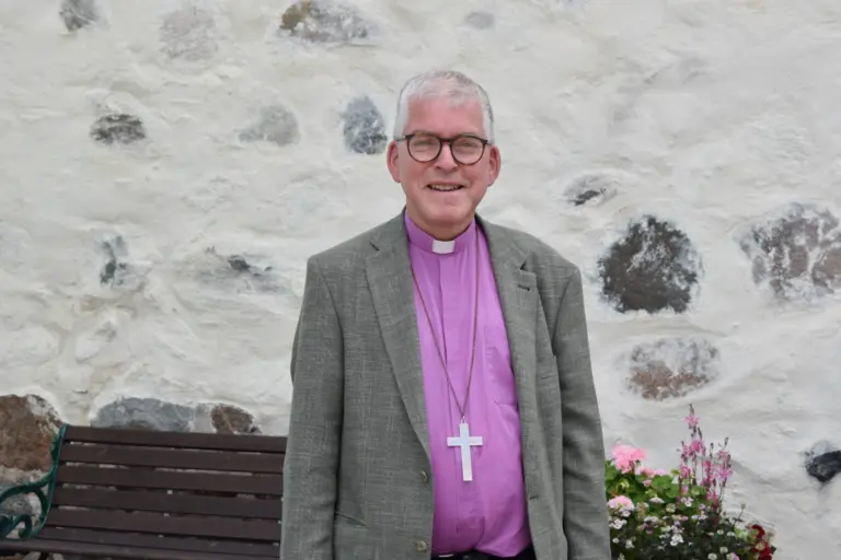 Biskop i grå kavaj framför kyrka