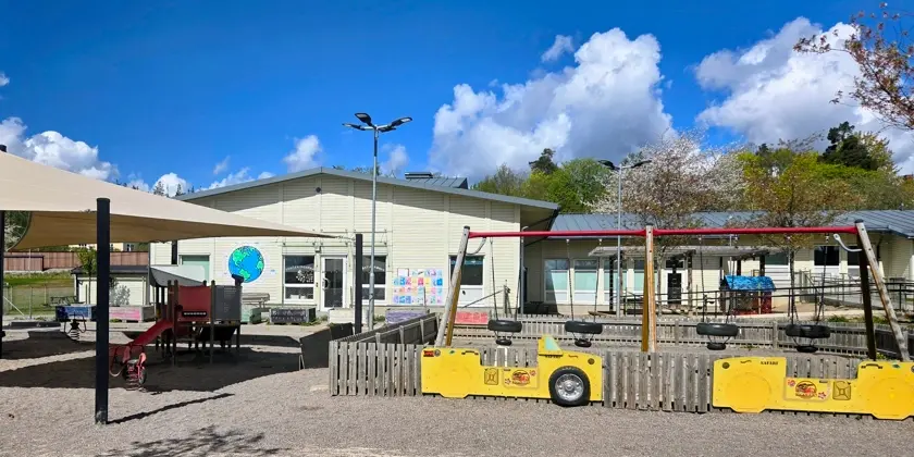 Lekplats framför förskolans låga vita byggnad.