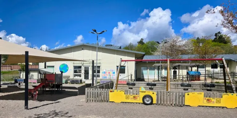 Lekplats framför förskolans låga vita byggnad.