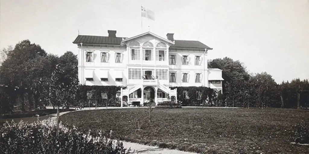 Ett svartvitt foto av en vit herrgård med flagga på taket.