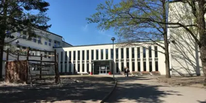 En stor skolbyggnad med träd och lekplats i förgrunden.