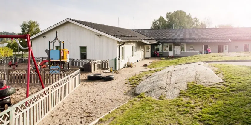 Ett lågt vinklat hus med en lekplats på tomten.