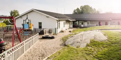 Ett lågt vinklat hus med en lekplats på tomten.