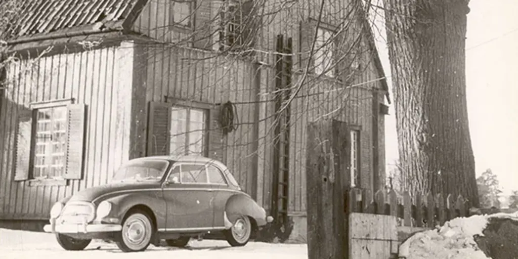 Ett svartvitt foto av en bil som står parkerad framför ett hus.
