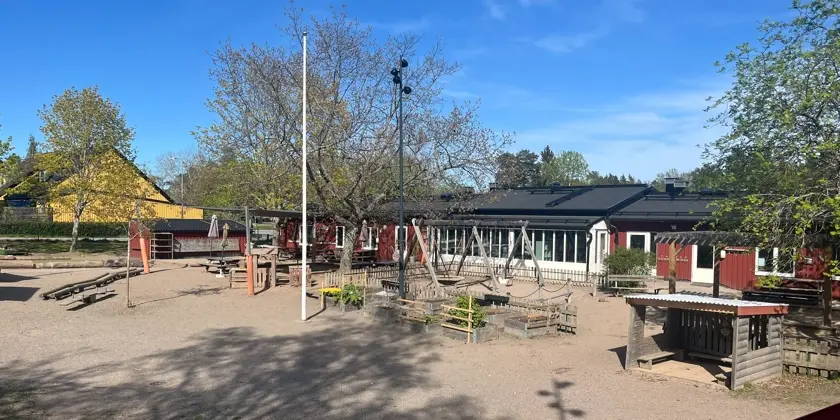 Låg byggnad med en lekplats och lekredskap.