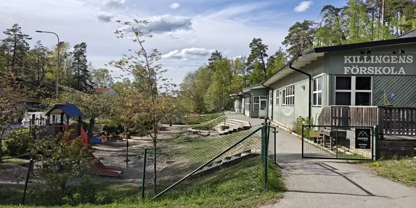 Ljusgrön låg byggnad med lekplats och omgiven av ett staket.