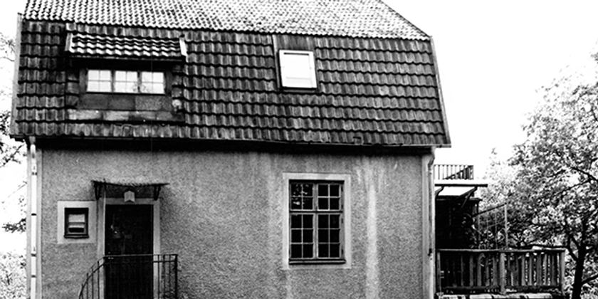Ett svartvitt foto av ett hus med en bil parkerad framför.