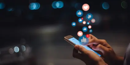 En person som använder en mobiltelefon med ikoner för sociala medier som sticker ut från den.