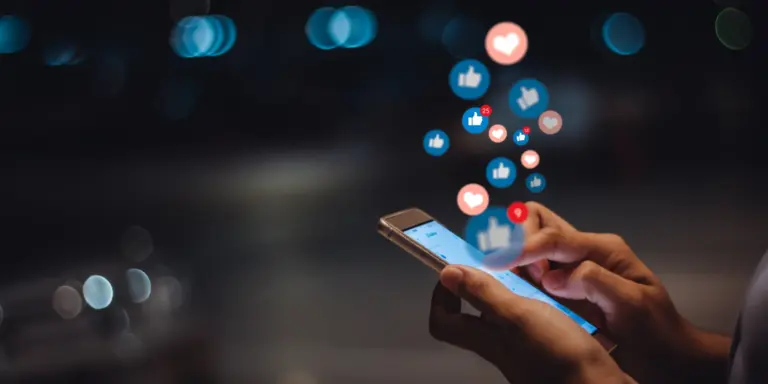 En person som använder en mobiltelefon med ikoner för sociala medier som sticker ut från den.