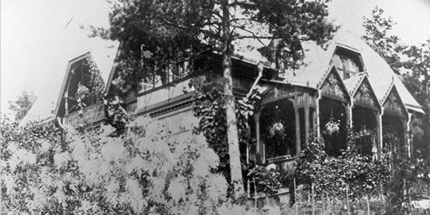 Ett svartvitt foto av ett hus omgivet av träd och grönska.