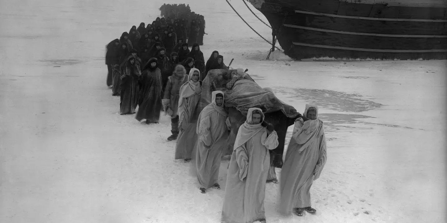 En grupp människor bärandes på en bår framför en båt.