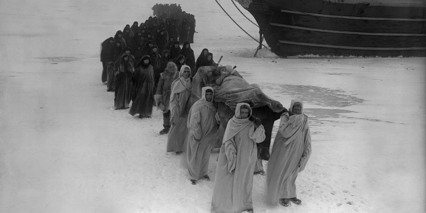 En grupp människor bärandes på en bår framför en båt.