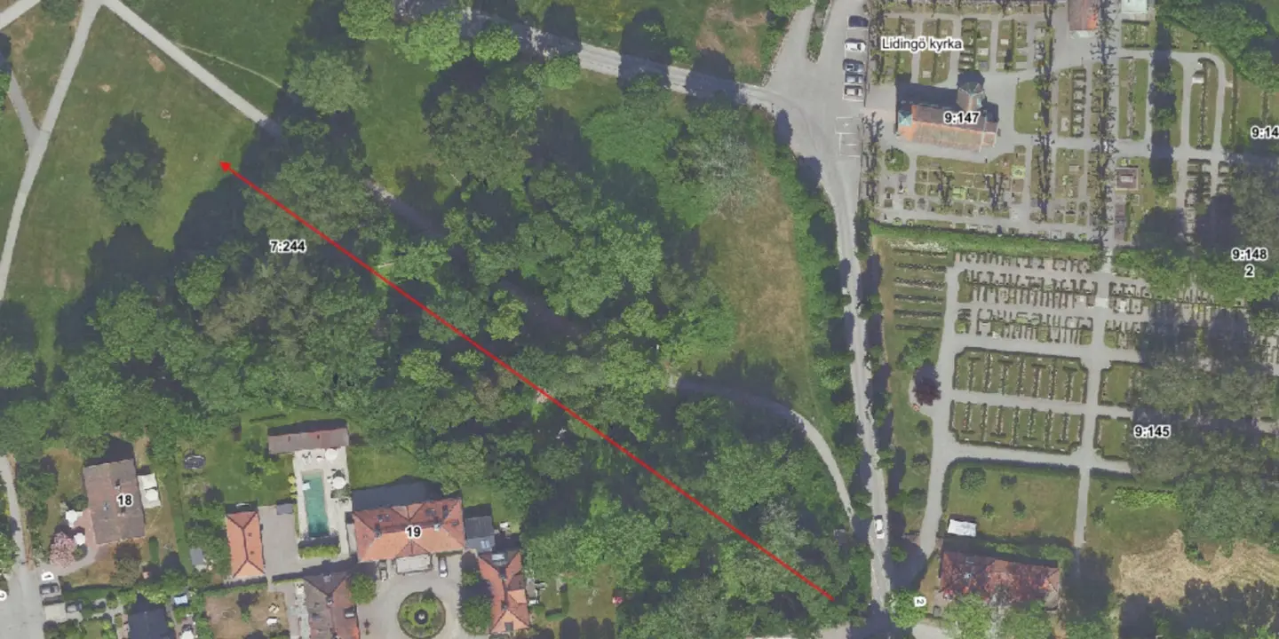 En flygbild över Kyrkviken, Lidingö kyrka och ett skogsområde med en röd pil över.