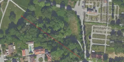 En flygbild över Kyrkviken, Lidingö kyrka och ett skogsområde med en röd pil över.